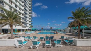 A hotel pool area with multiple lounge chairs and palm trees, surrounded by a white building with balconies. - Stunning Penthouse on Hollywood Beach (Hollywood)