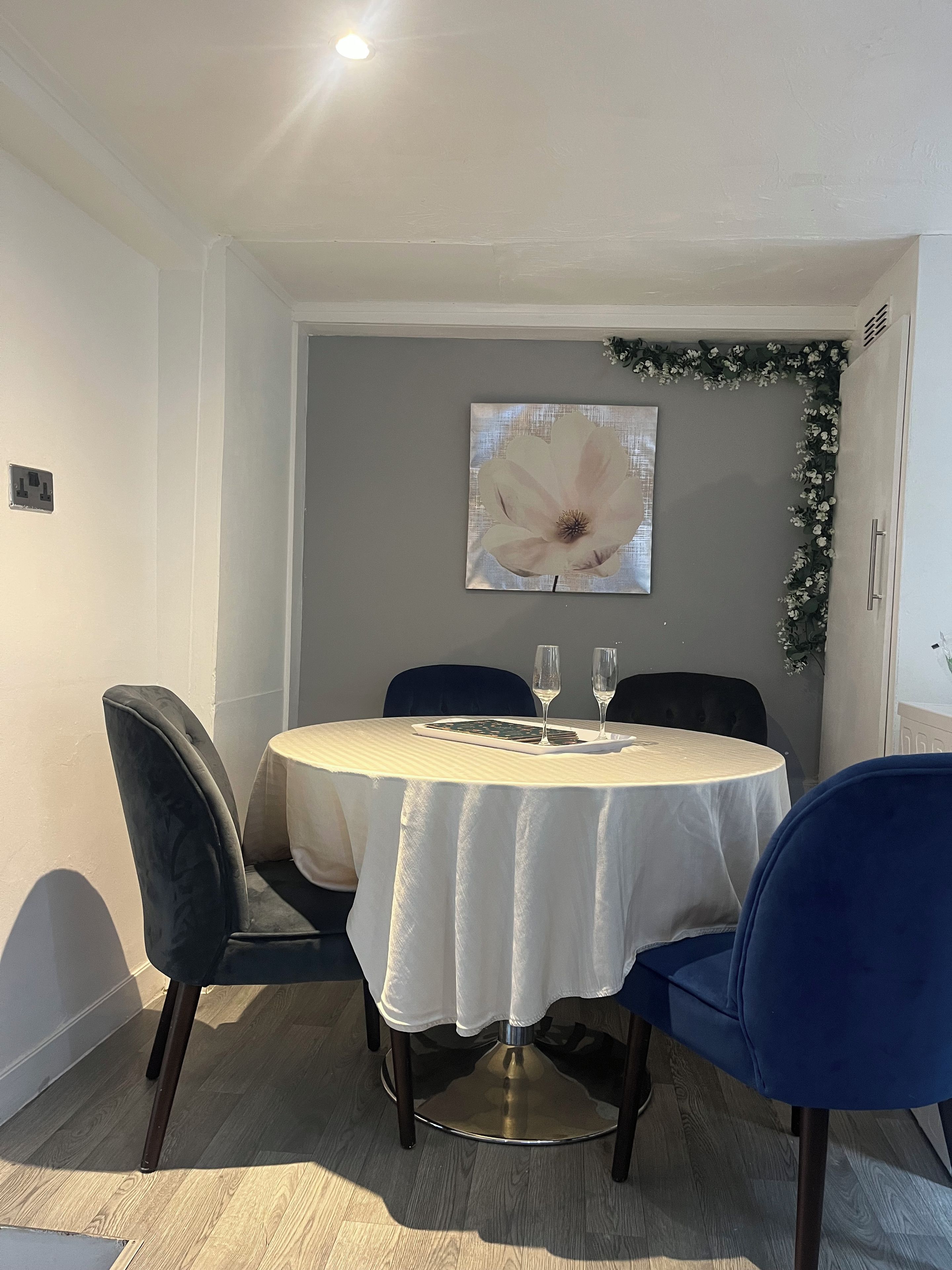 Un comedor con una mesa redonda, dos sillas y un cuadro de flores colgado en la pared.