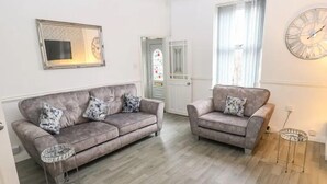 Ein Wohnzimmer mit zwei grauen Sofas, einem kleinen runden Tisch und einem großen Fenster mit Vorhängen.