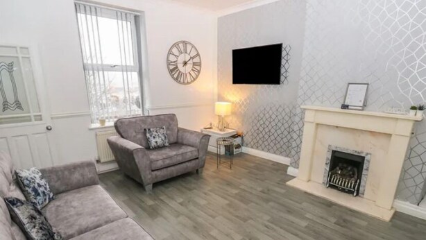 Ein Wohnzimmer mit grauem Sofa, einem kleinen Sessel, einem runden Couchtisch und einem Kamin.