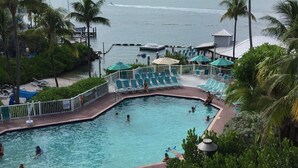 Ein Poolbereich mit Liegestühlen und Sonnenschirmen, Blick auf das Meer und eine entfernte Insel.