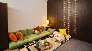A cozy living room with a green sofa, decorative pillows, a small side table with a lamp, and a string of lights on the wall.