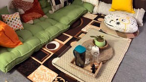 A cozy living room with a green sofa, various pillows, a small coffee table with drinks and a plant, and a lamp.
