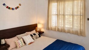 A bedroom with a bed, a ceiling fan, a window with curtains, and a wall decoration.