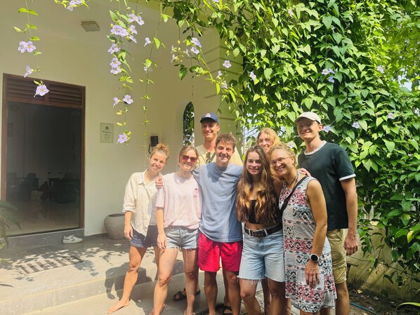 Un groupe de personnes se tient devant un bâtiment orné d’une vigne verte et de fleurs violettes.