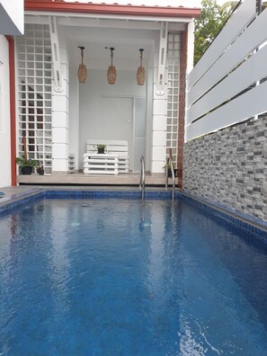 Une piscine dont le bord est recouvert de carreaux, avec un banc blanc et un mur en pierre.