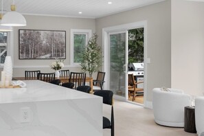 A modern kitchen with a white marble countertop, a dining area with a wooden table and chairs, and a sliding glass door leading to a patio. - Charming Riverside Retreat in the Heart of Huntsville (Huntsville)
