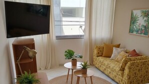 A hotel room with a bed, a sofa, a TV, a desk, and a window with curtains.