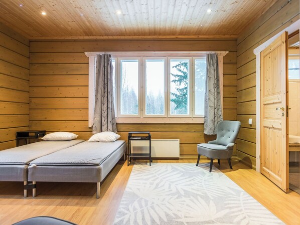 Une chambre de style cabane avec deux lits, une chaise, une fenêtre avec des rideaux et un radiateur.