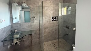 Uma casa de banho moderna com cabine de chuveiro em vidro, lavatório em vidro e painel de parede em mármore.