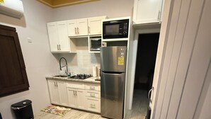 Uma cozinha compacta com armários brancos, uma geladeira de aço inoxidável, um micro-ondas e um fogão a gás.