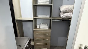 Armário compacto e bem organizado, com prateleiras, gavetas e espaço para pendurar, com máquina de lavar e cama com almofadas.