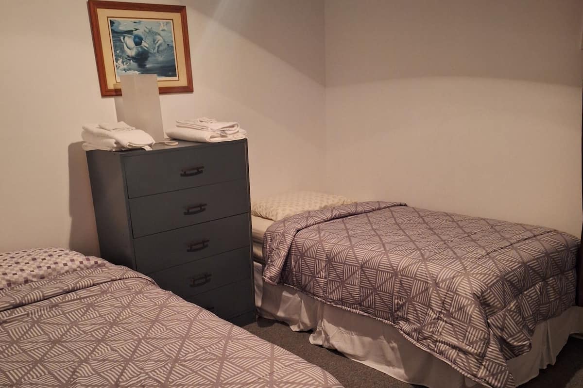 A hotel room with two beds, a dresser, and a painting on the wall.