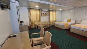 Une chambre d’hôtel avec deux lits, un bureau, une chaise, une petite table et une fenêtre avec des rideaux.
