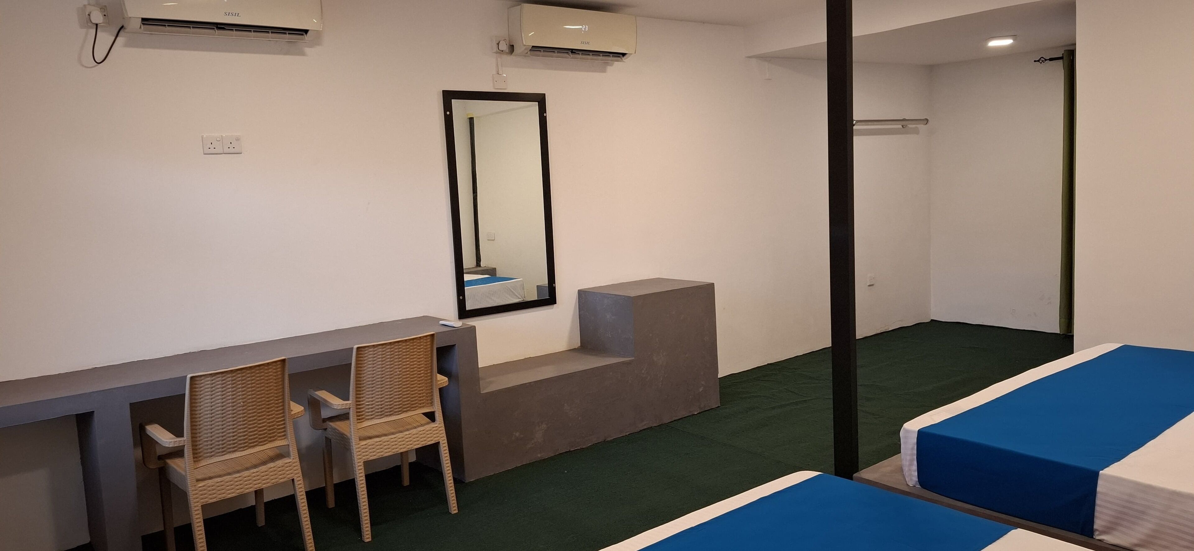 Ein Hotelzimmer mit Schreibtisch, zwei Stühlen, einem Spiegel, einem Bett mit blauer Bettwäsche und einem grünen Teppich.