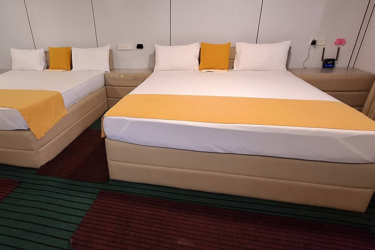 Ein Hotelzimmer mit zwei Betten, jeweils mit einer gelben Tagesdecke, und einem Nachttisch mit einer Lampe.