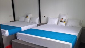 Deux lits simples avec une literie blanche et des têtes de lit bleues, un oreiller blanc orné d’un logo et un rideau vert sur le côté droit.