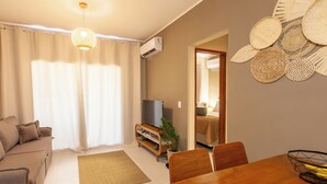 Ein modernes Wohnzimmer mit Sofa, TV-Schrank, Esstisch und Wandbildern.