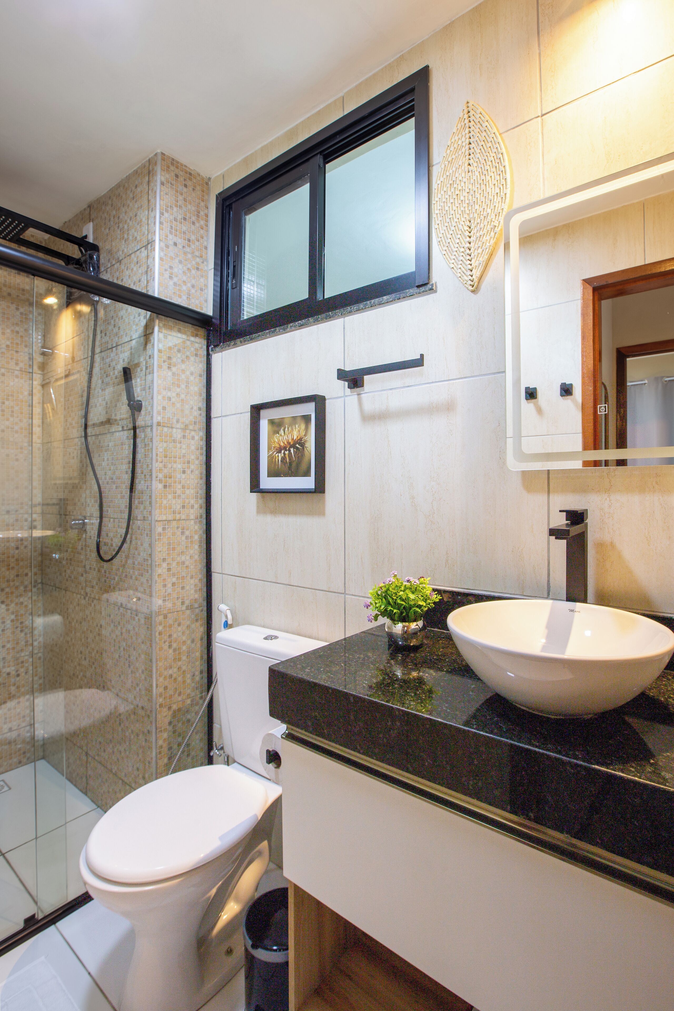 A modern bathroom with a glass shower enclosure, a white toilet, a large sink, and a small potted plant.