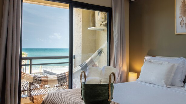 Ein Hotelzimmer mit Bett, Fenster mit Meerblick, einer Hängematte und einem Korb mit Handtüchern.