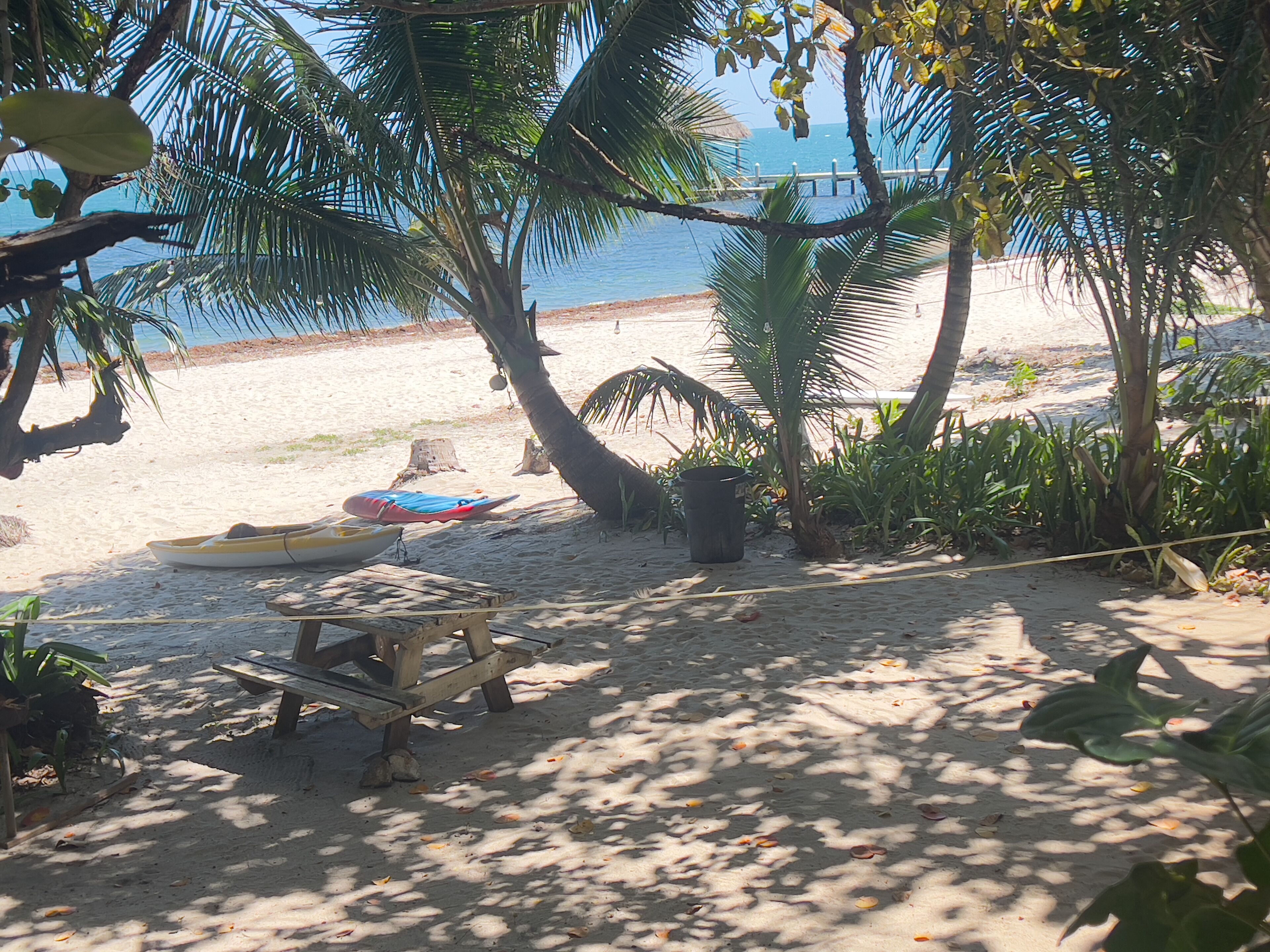 A beach with a wooden bench, a yellow boat, and a blue kayak.