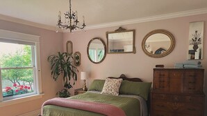 A bedroom with a large bed, a dresser, a chandelier, and multiple mirrors.