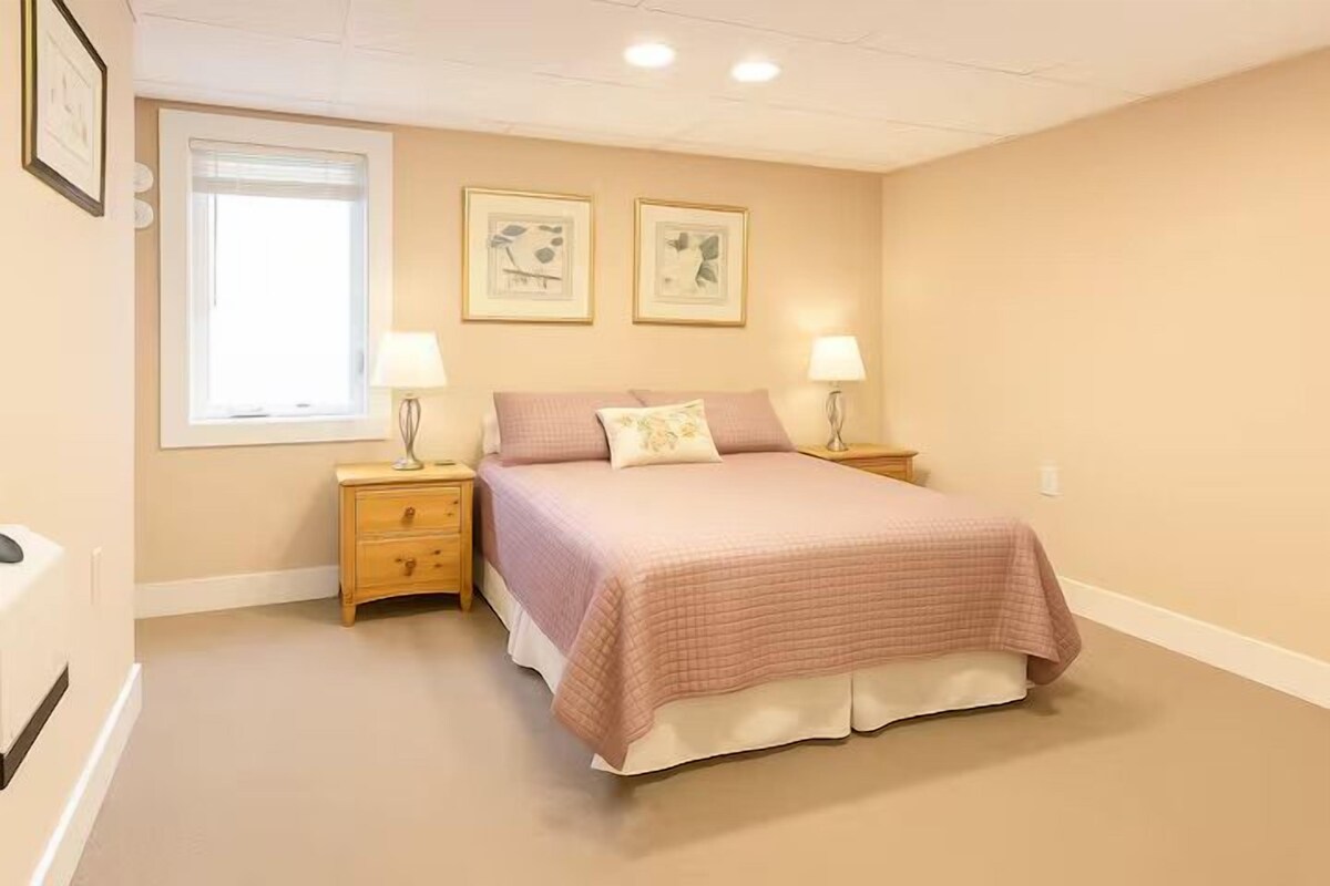 A bedroom with a bed, two bedside tables, a window, and wall-mounted artwork.