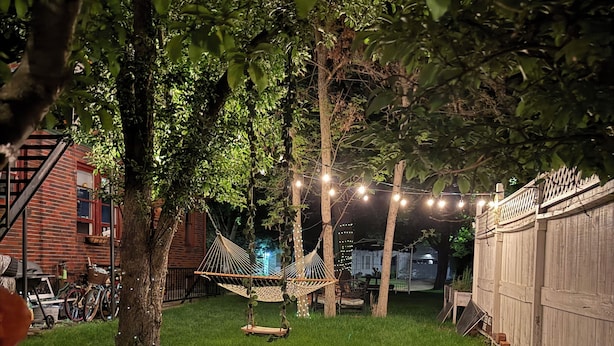 A backyard with a hammock, wooden deck, and string lights.