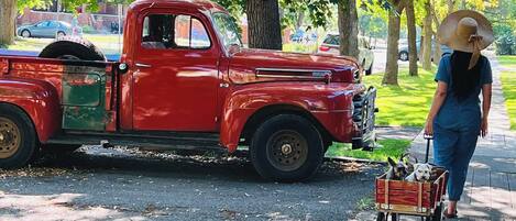 A red vintage truck parked on a street with a woman pushing a dog cart.