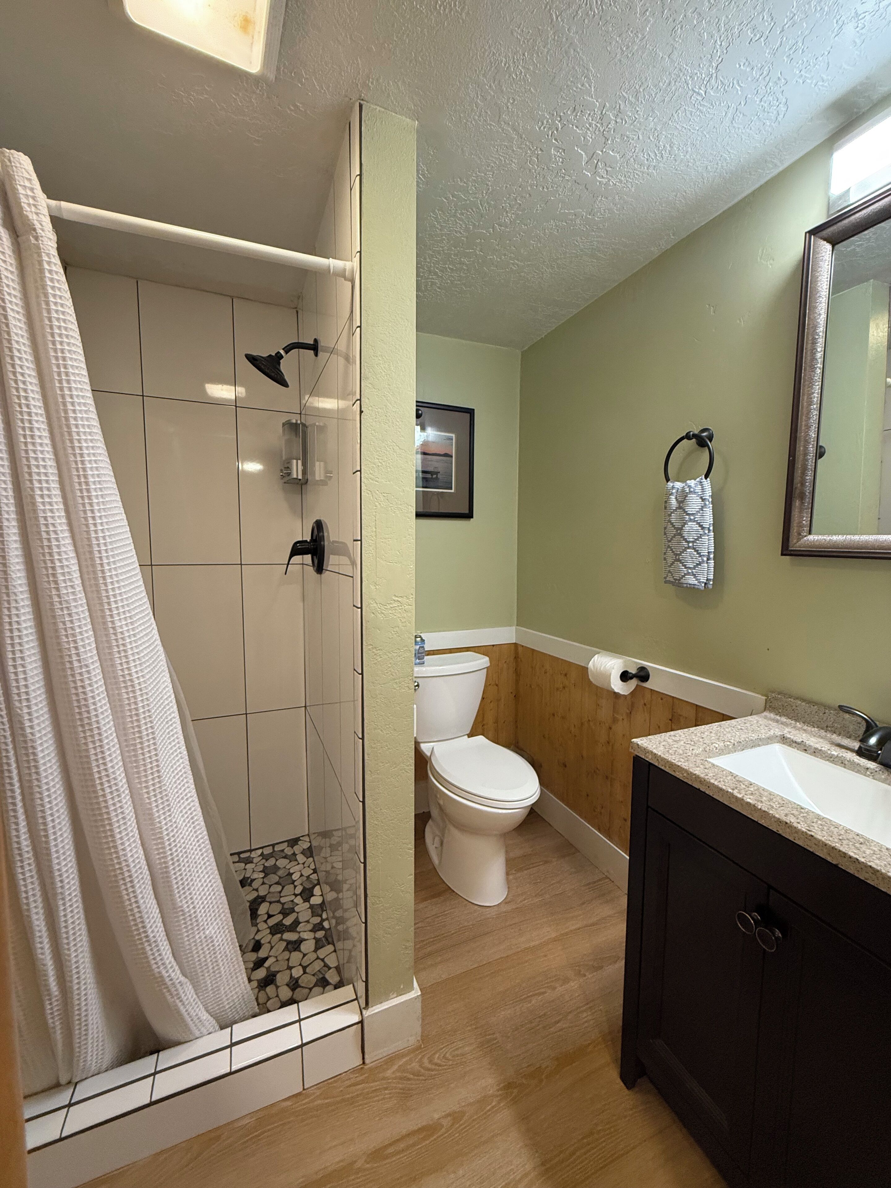 Une salle de bain avec douche, toilettes, lavabo et plancher en bois.