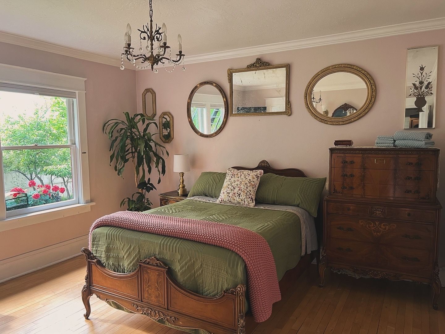A bedroom with a large bed, a dresser, a chandelier, and multiple mirrors.