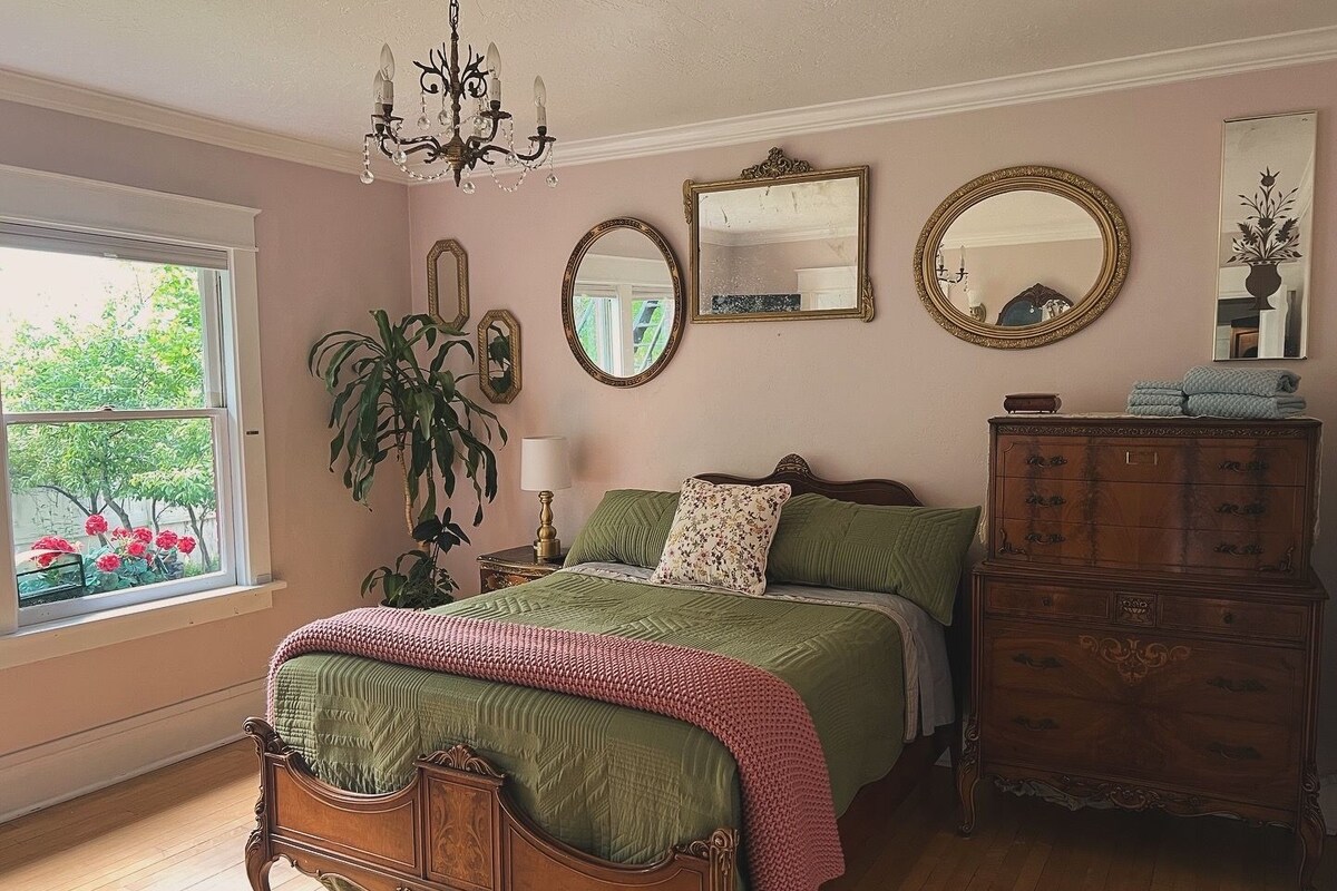 A bedroom with a large bed, a dresser, a chandelier, and multiple mirrors.