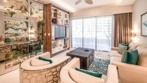 A modern living room with a sofa, a coffee table, a TV, and a bookshelf. - Spacious 1‑bedroom suite, complete with premium 5‑star, resort‑style amenities. (Cabo San Lucas)