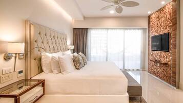 A modern hotel room with a large bed, a ceiling fan, a TV mounted on the wall, and a window with curtains.