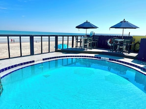 Una piscina con límite de profundidad de 1.2 metros, junto a una playa con valla, y mobiliario exterior con sombrillas.