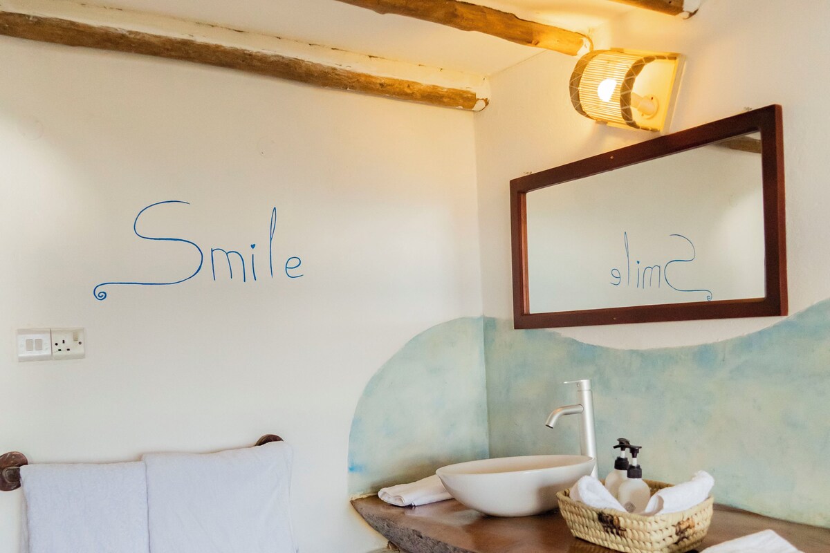 Une salle de bain avec un plafond en bois, un lavabo blanc avec un bac, un porte-serviettes et un miroir avec une lampe au-dessus.