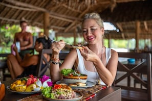 A person sitting at a table with a meal, including a bowl of salad and various fruits. - Veridiana Hotel (Kizimkazi)