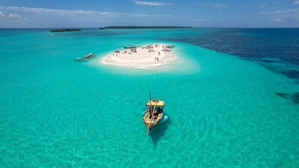An aerial view of a small island with clear turquoise waters, a boat in the foreground, and a distant island. - Veridiana Hotel (Kizimkazi)