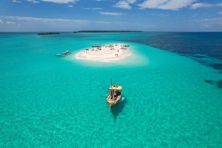 An aerial view of a small island with clear turquoise waters, a boat in the foreground, and a distant island.. Veridiana Hotel