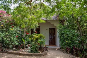 A house with a thatched roof, surrounded by lush greenery and flowering plants. - Veridiana Hotel (Kizimkazi)