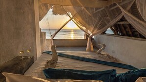 A bed with a view of the sunset over the ocean, a swan sculpture, and two glasses of wine on a bedside table. - Veridiana Hotel (Kizimkazi)