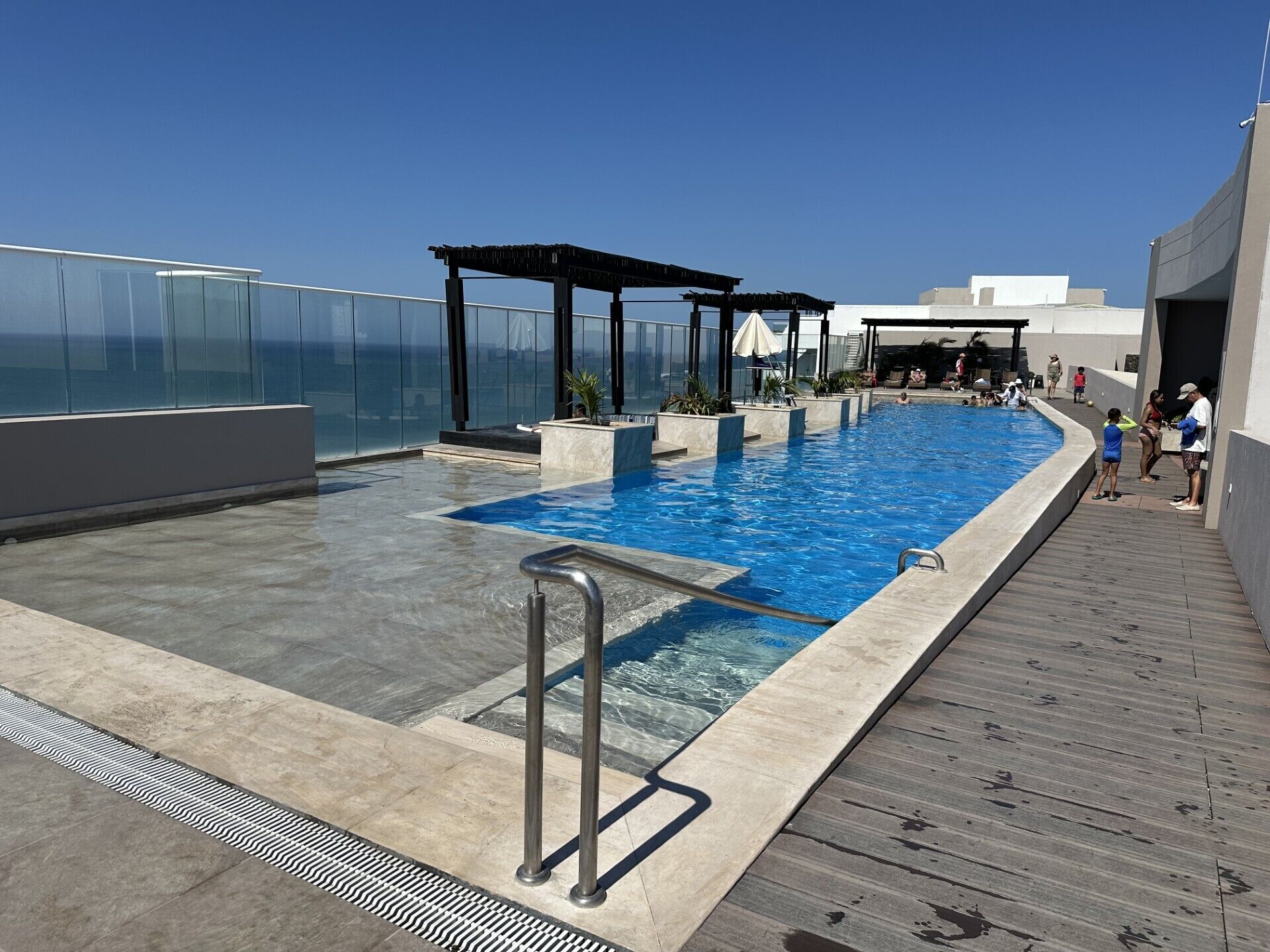 Une piscine sur le toit offrant une vue dégagée sur l’océan, une terrasse en bois et un espace salon couvert.