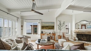 Un salon spacieux doté d’une cheminée, d’un ventilateur de plafond et de grandes fenêtres équipées de volets.