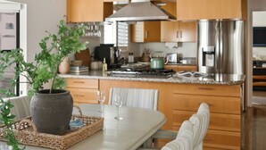 Une cuisine moderne avec des meubles en bois, des appareils en acier inoxydable et un coin repas comprenant une table blanche et des chaises à rayures.