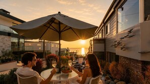 Une terrasse avec une table et des chaises, un parasol et une vue sur le coucher de soleil.