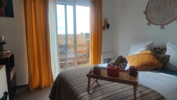 A bedroom with a bed, a bedside table with a lamp, a window with curtains, and a wall tapestry. - A sunny interlude (Galargues)