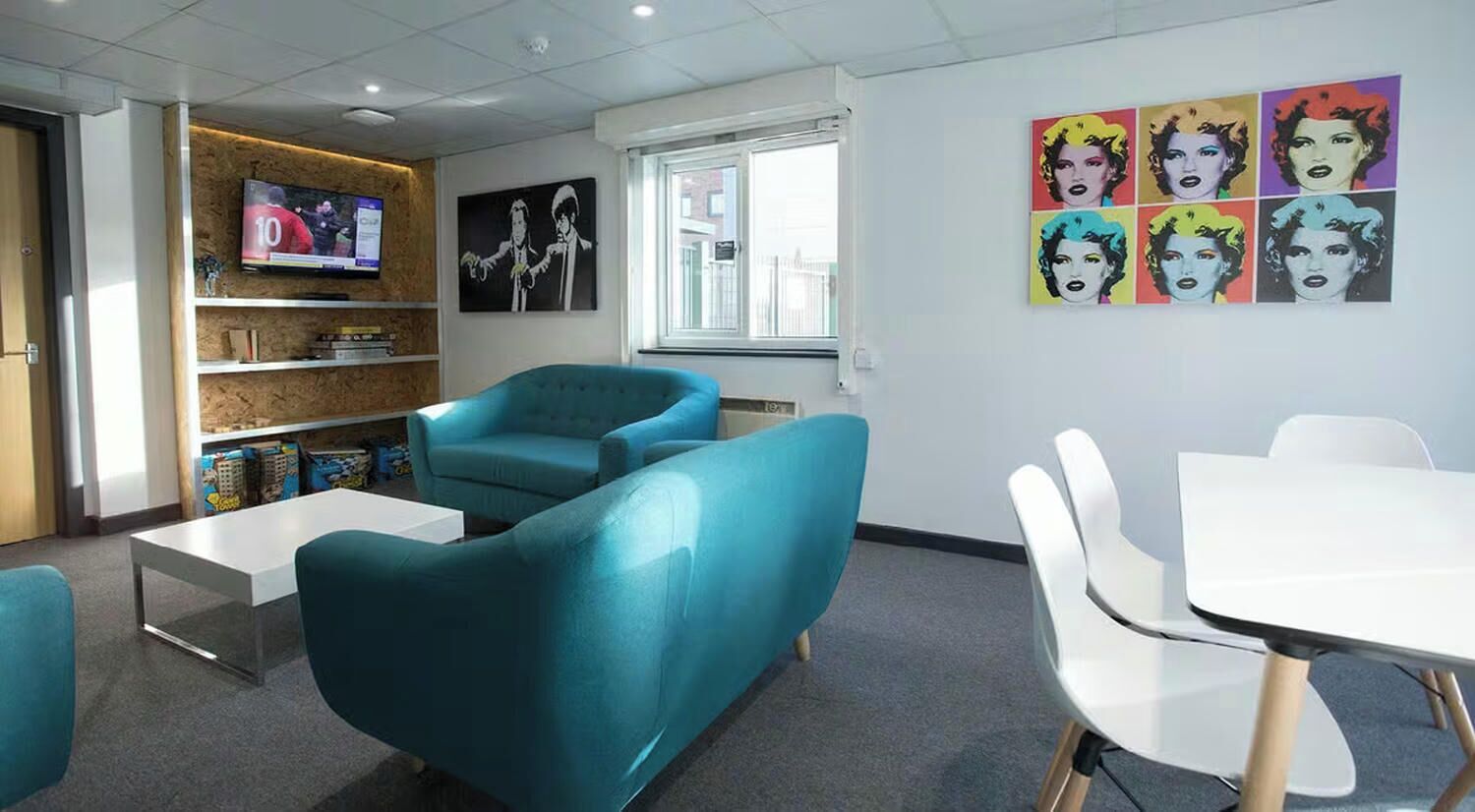A modern office space with teal chairs, a white table, and a TV on the wall.
