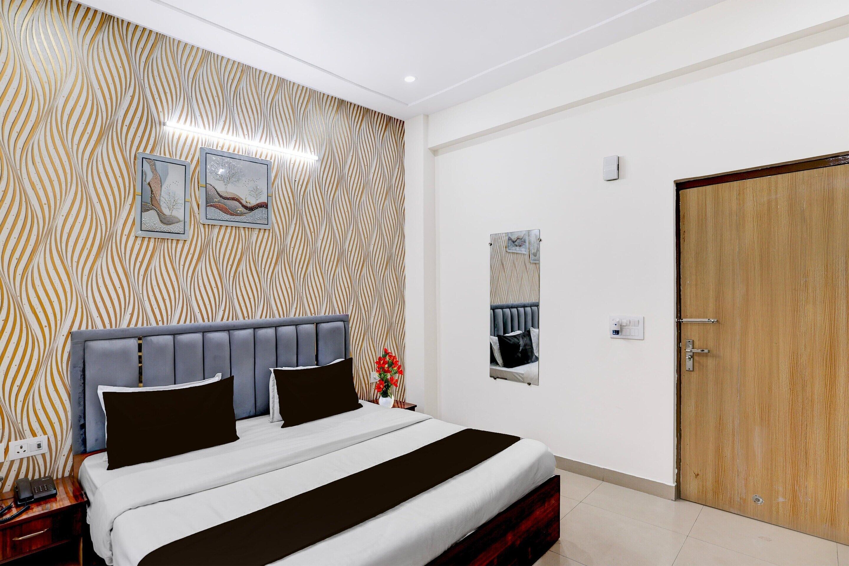 Un dormitorio ordenado con papel tapiz estampado, una cama con cabecera gris y una puerta de madera.