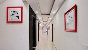 Un largo y estrecho pasillo con paredes blancas y suelo pulido. Hay obras de arte enmarcadas en las paredes y puertas que dan a otras habitaciones.