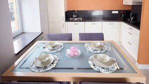 Une cuisine moderne avec des meubles blancs, un plan de travail noir et un coin repas doté d’une table à plateau en verre, préparée pour accueillir quatre personnes.